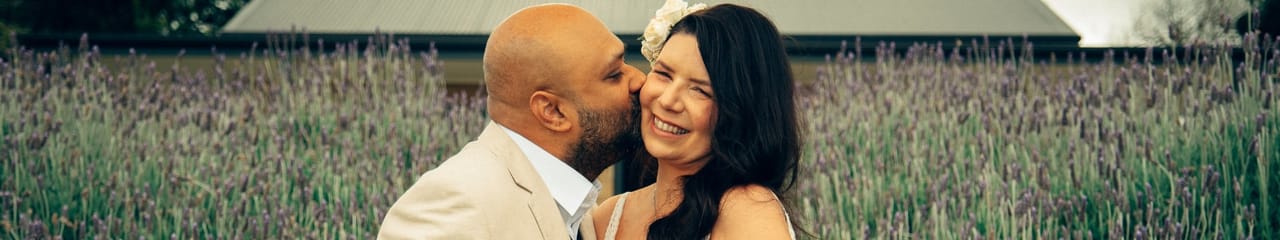 A groom kissing the bride on the cheek in a field of tall lavender