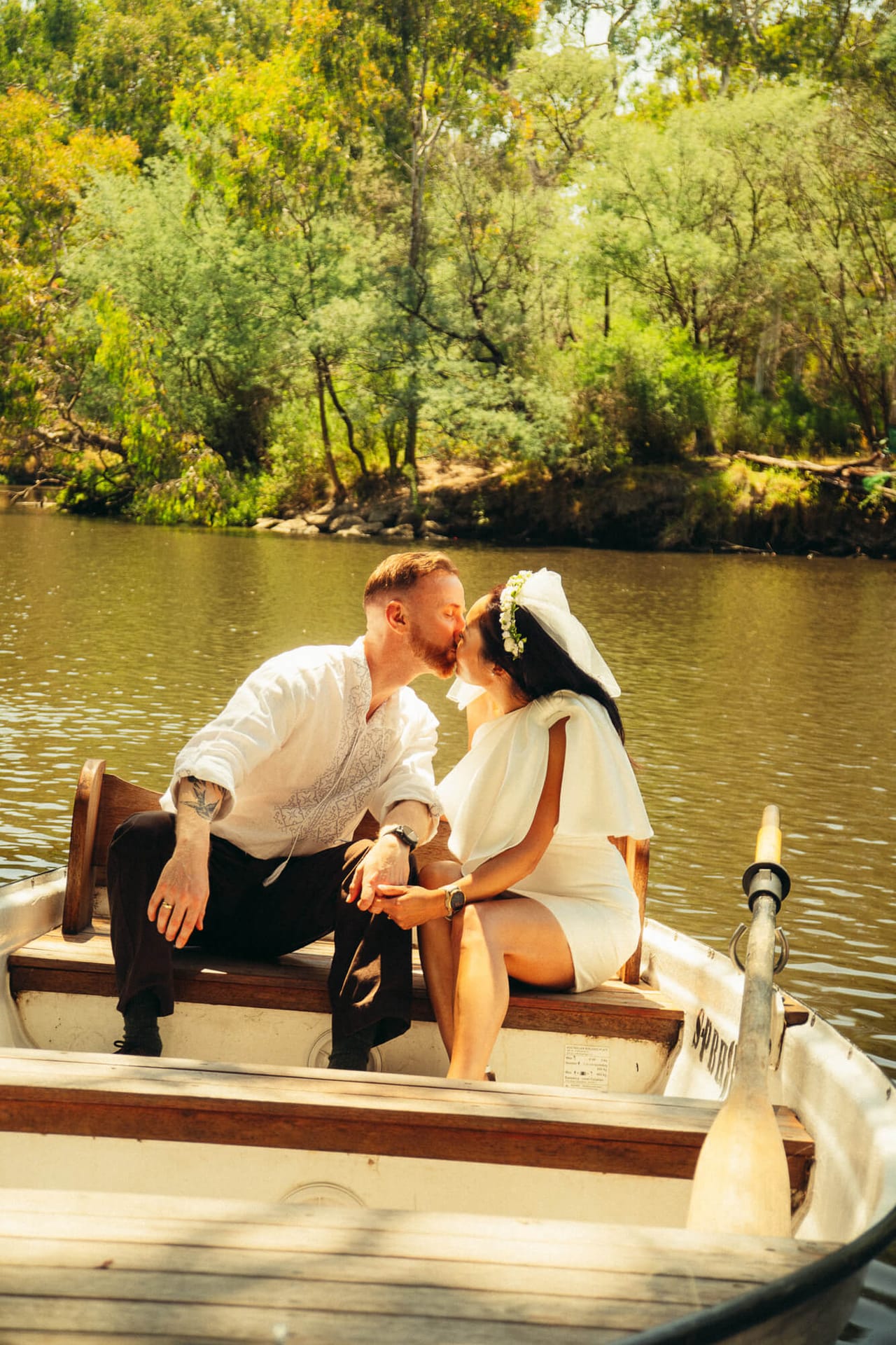 A couple kissing in a small rowing boat on a river lined with green trees