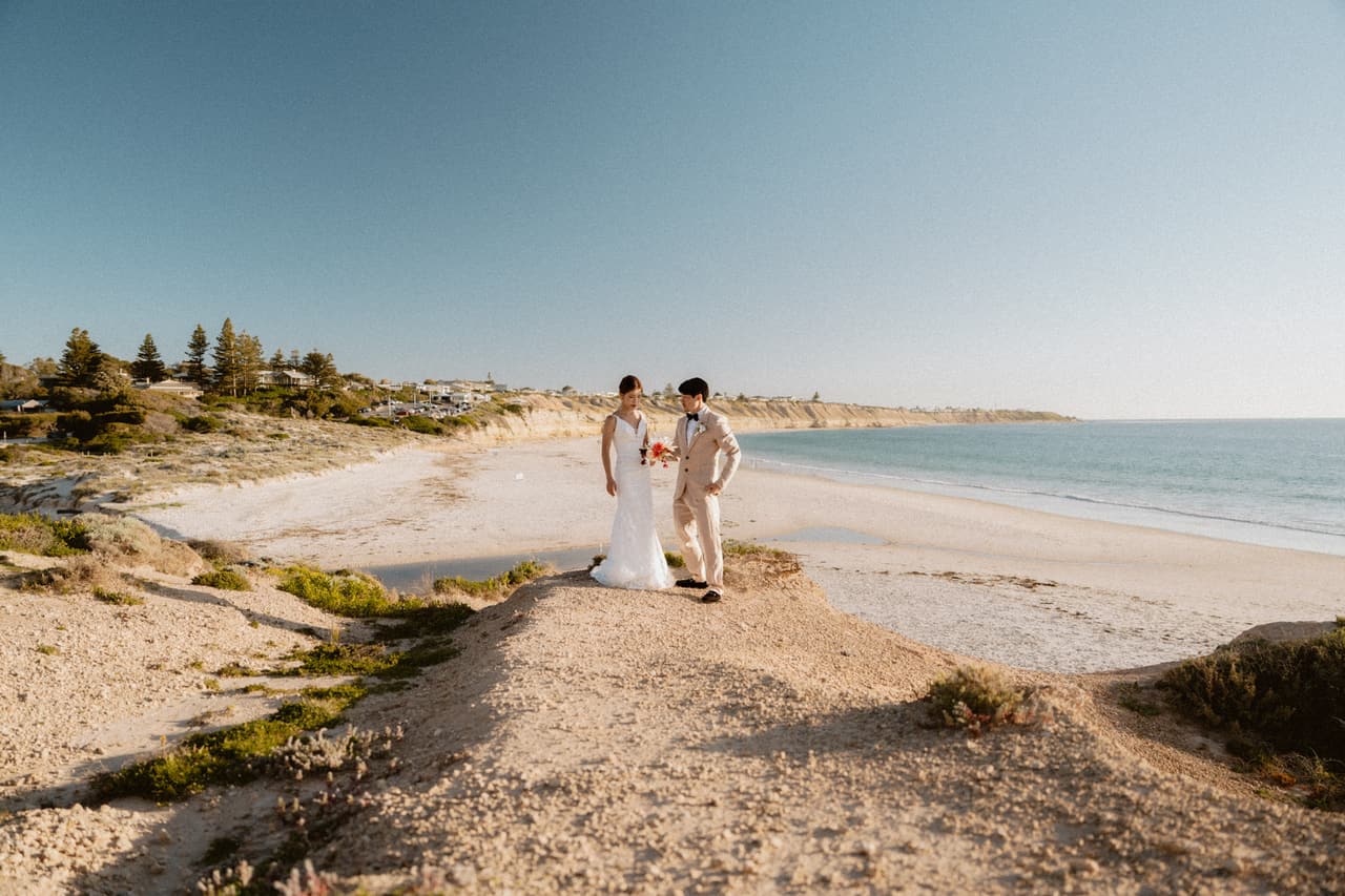 A couple standing on a sandy point above a long curving beach in afternoon sun