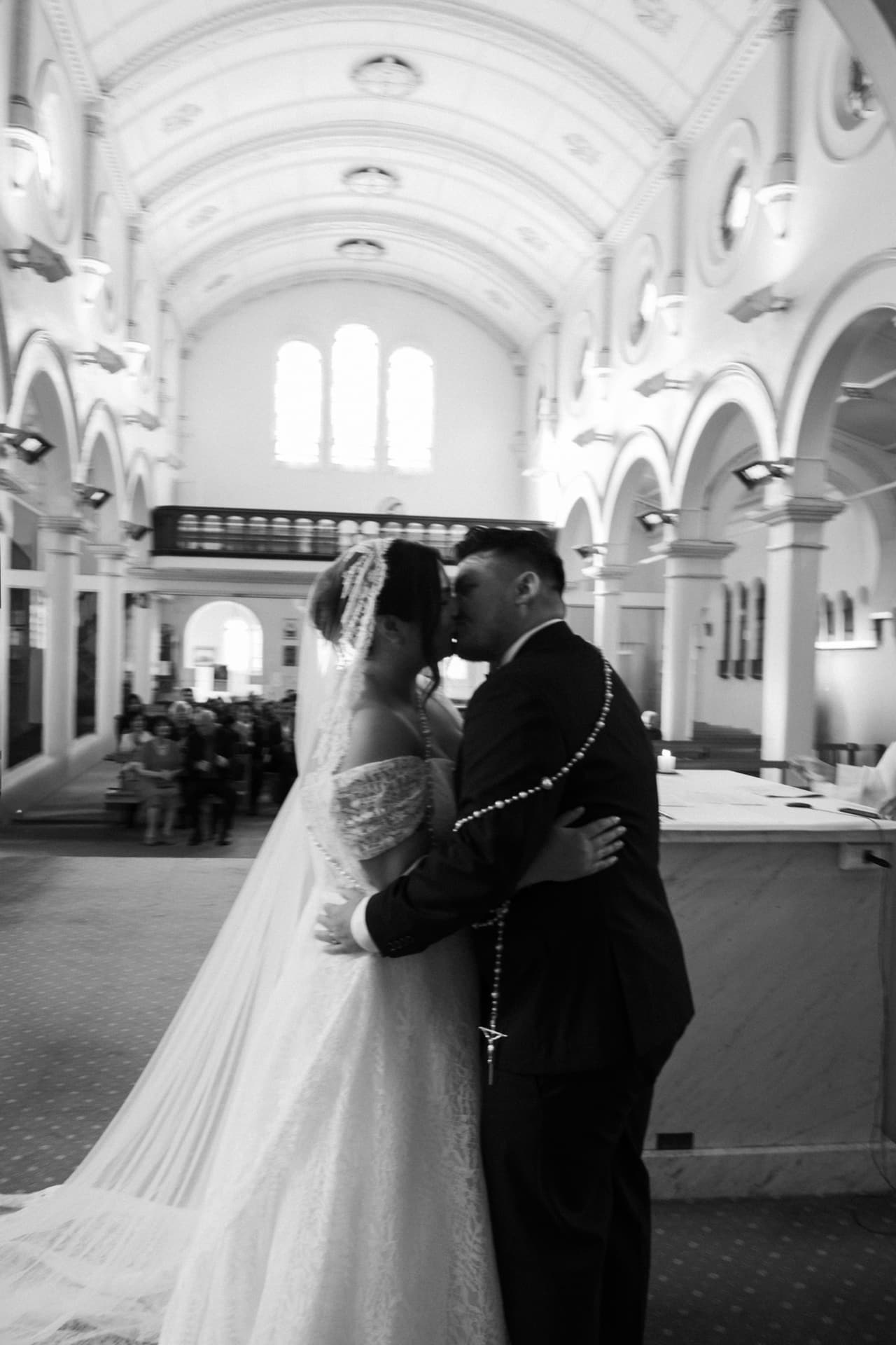 Black and white photo of a couple kissing at the front of a vaulted church