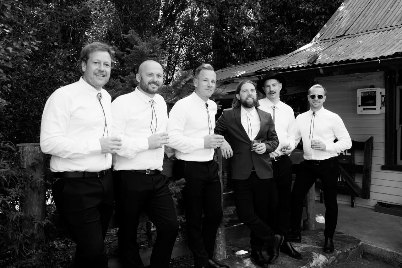 Black and white photo of groomsmen in white shirts laughing outside a country hotel