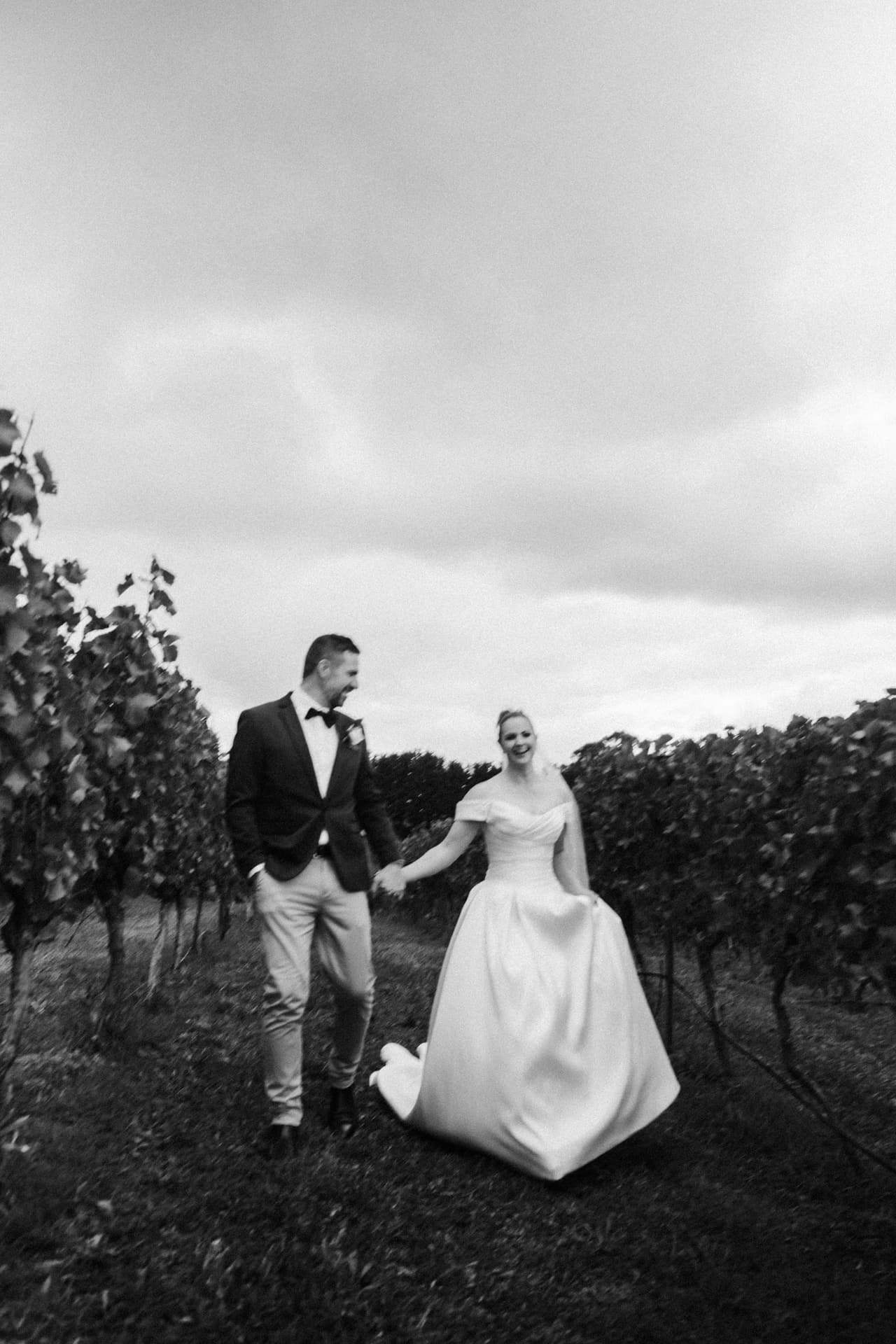 Black and white photo of a couple walking hand in hand between rows of vines