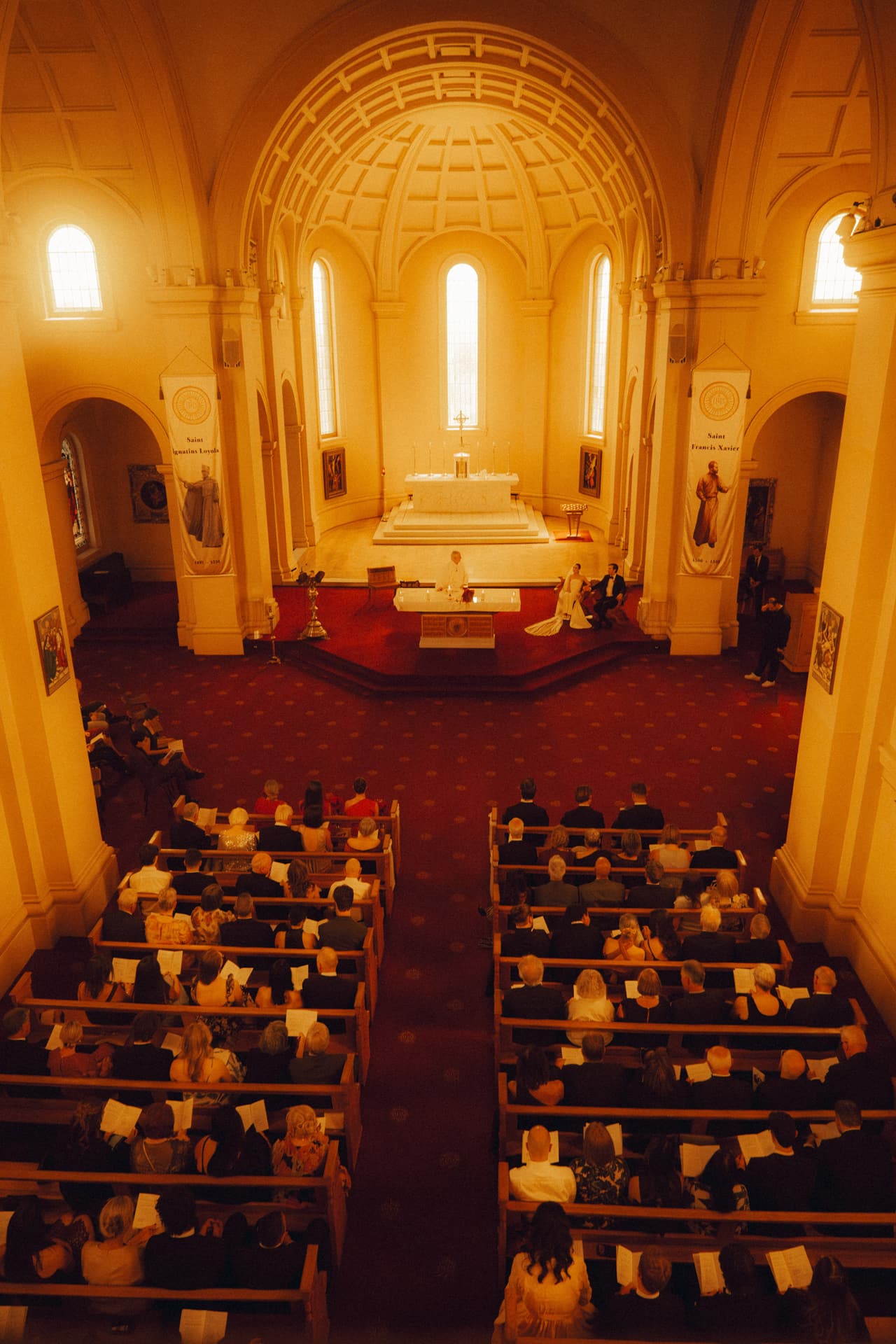 A church ceremony seen from the balcony, guests filling the pews in warm afternoon light