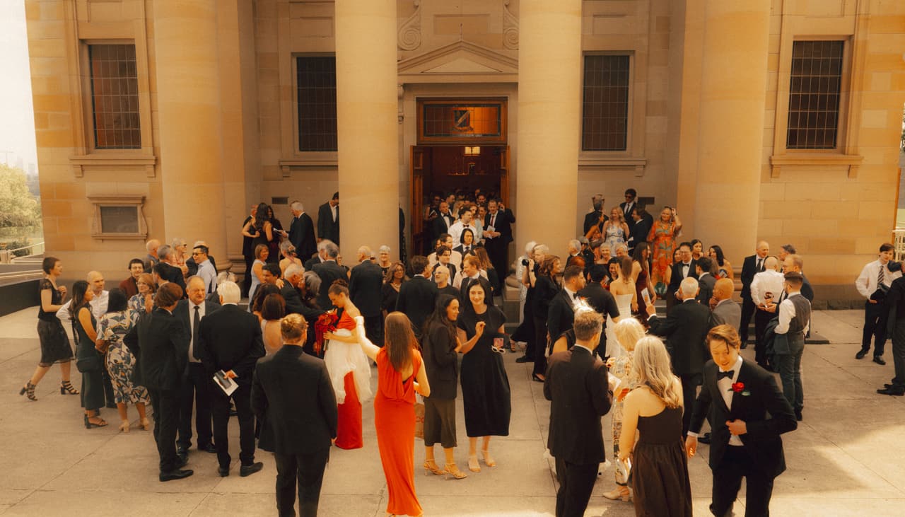 Wedding guests gathering outside a sandstone church after the ceremony, seen from above