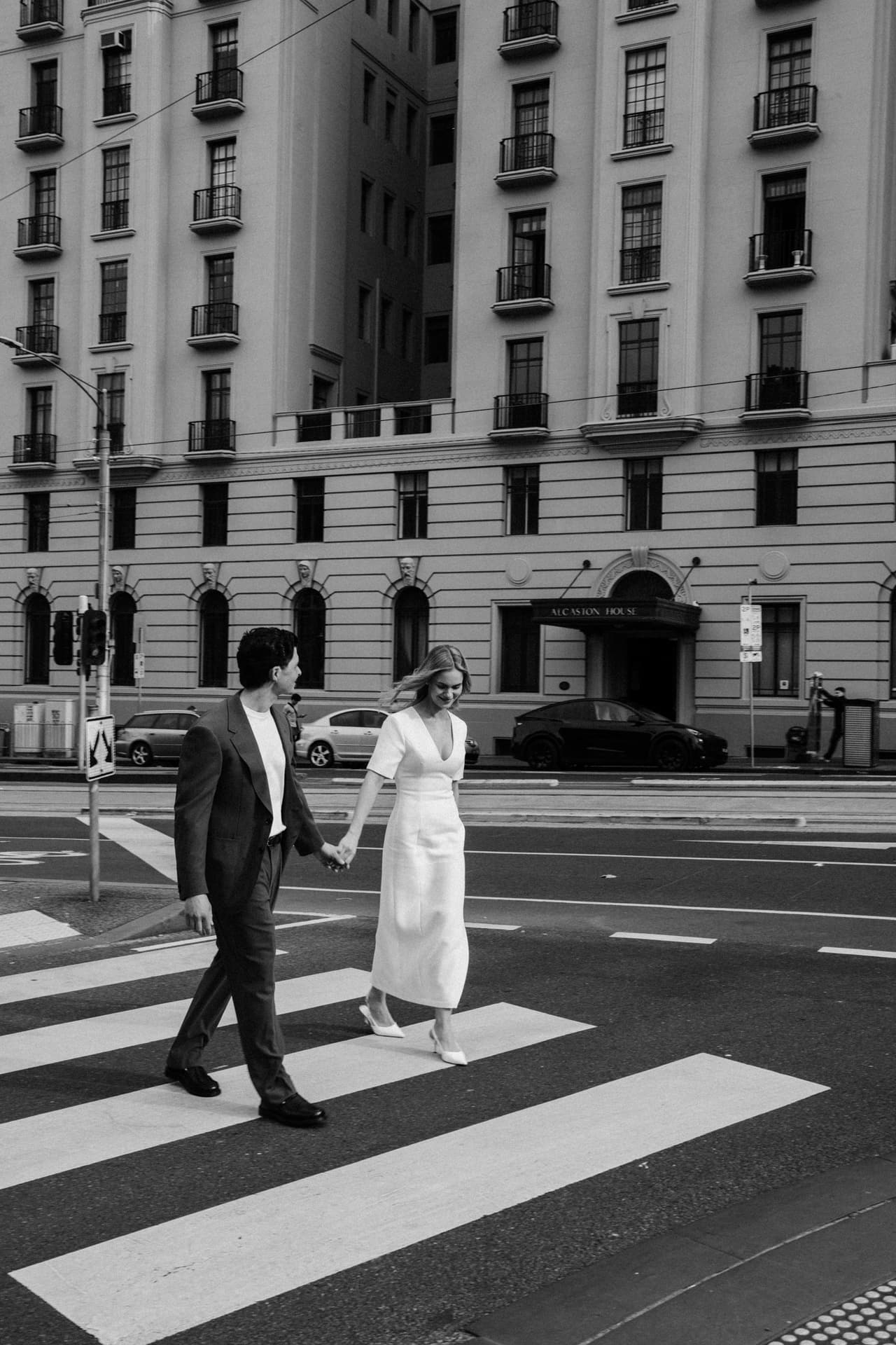 Black and white photo of a couple crossing a city street hand in hand at a zebra crossing