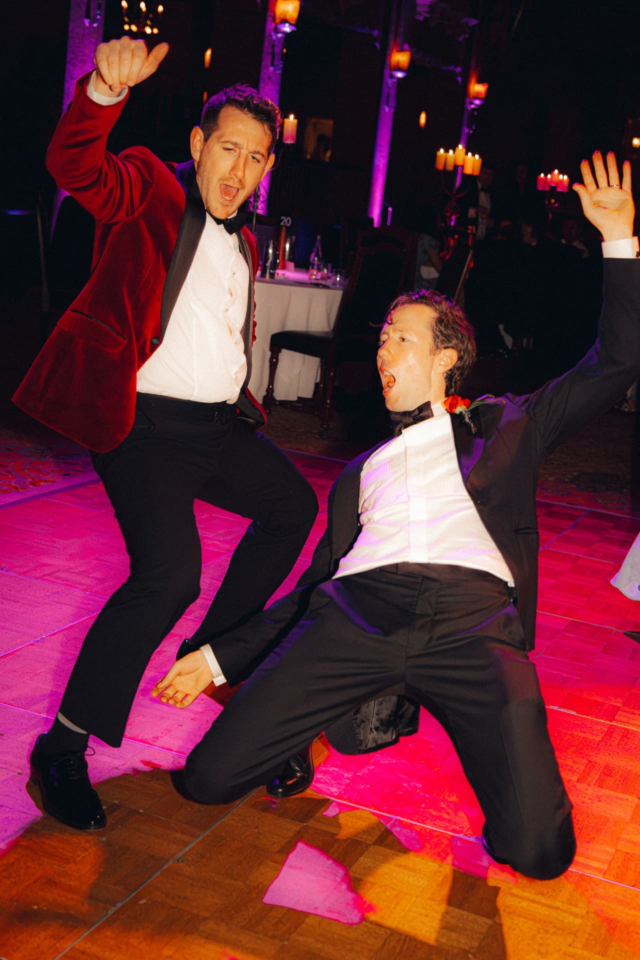 Two guests in tuxedos dancing wildly on a dance floor lit pink and red