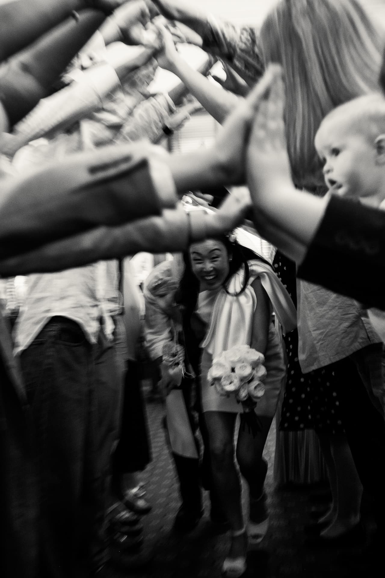 Black and white photo of a child ducking through a tunnel of guests’ raised hands
