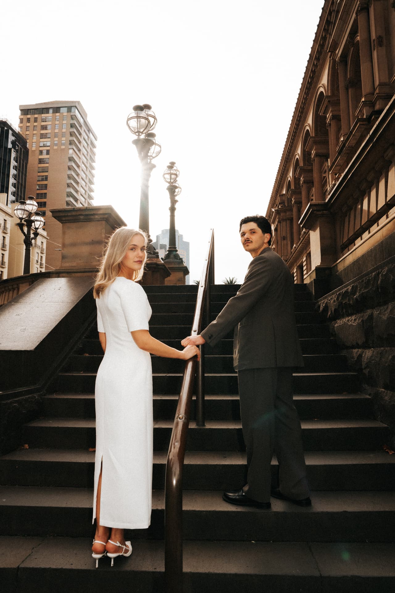 A couple holding hands on a city staircase, the bride looking back at the camera