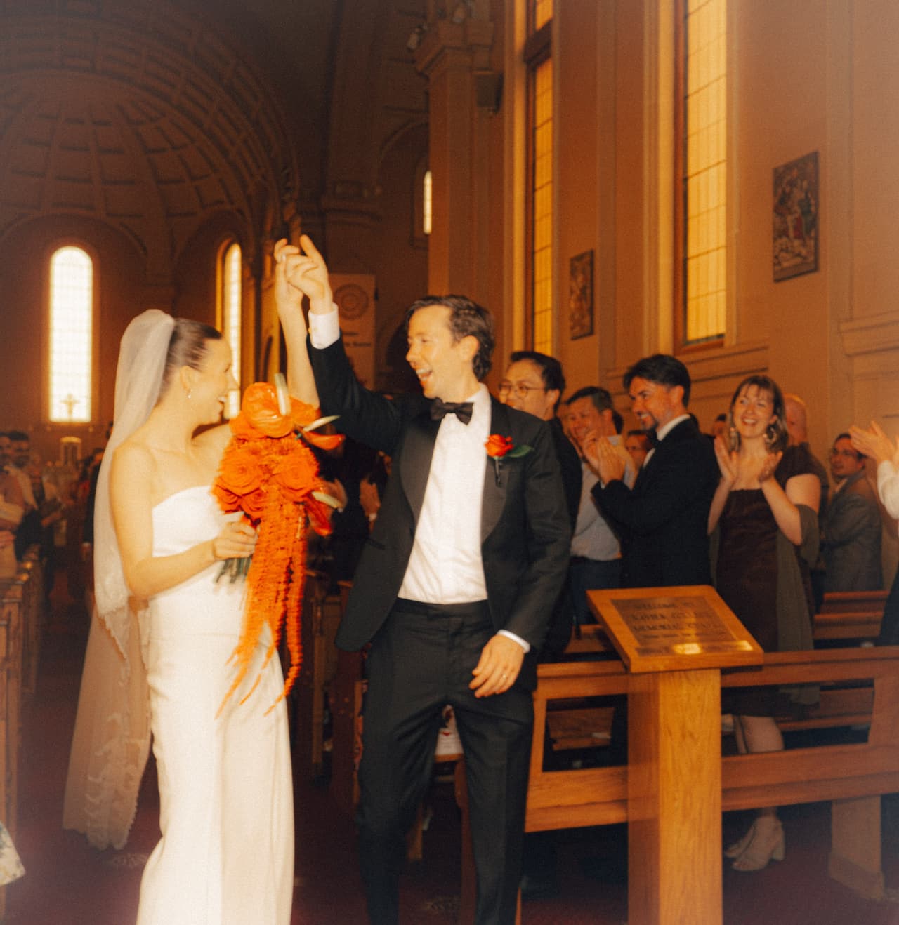A groom raising his fist as he and the bride walk back down the aisle while guests clap