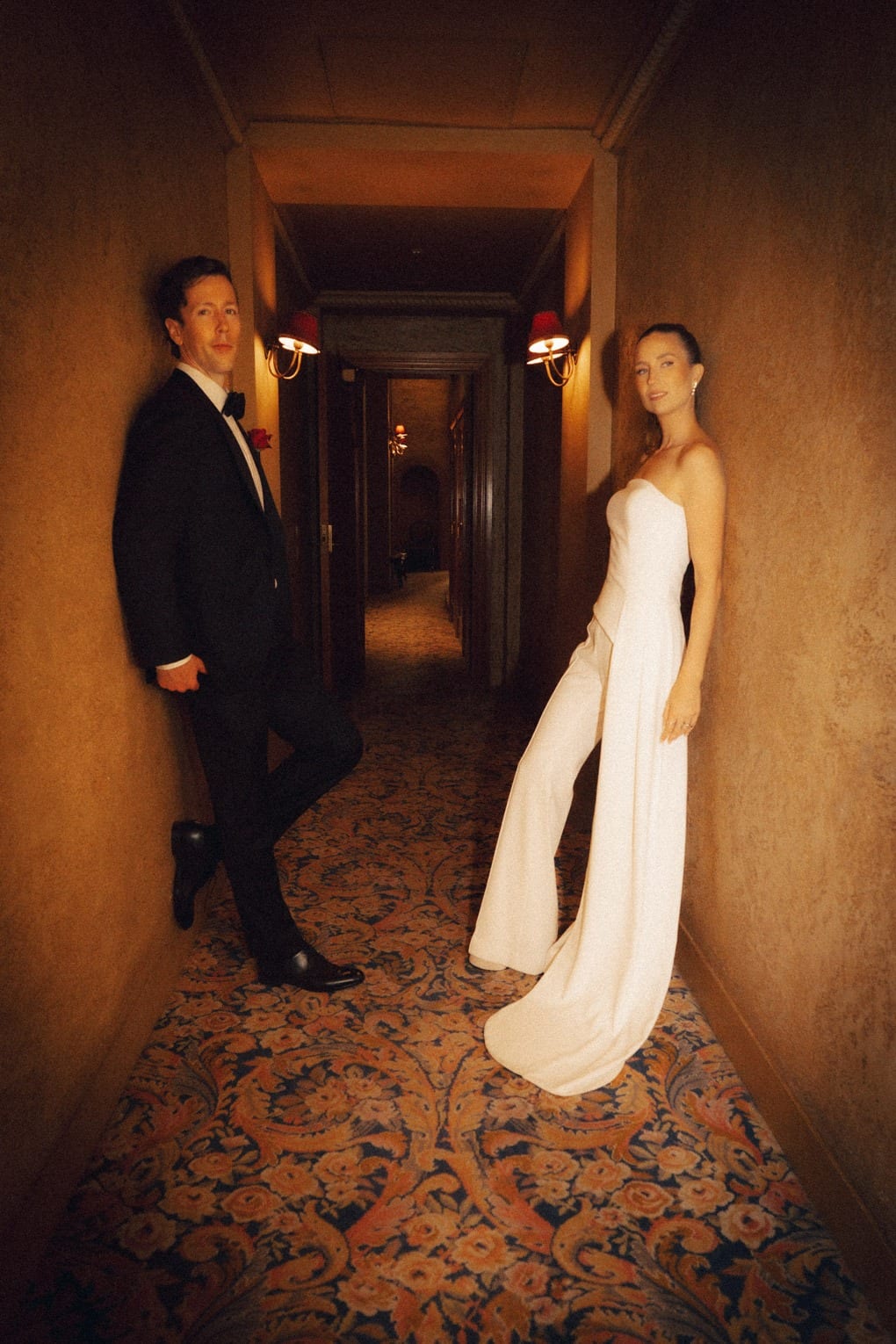A couple leaning on opposite walls of a narrow, warmly lit theatre corridor