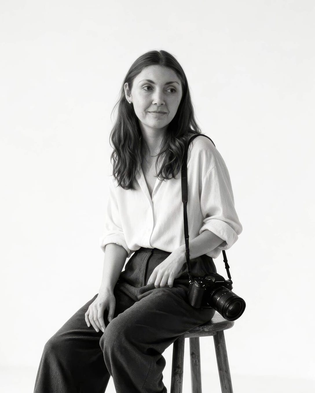 Megan, Adelaide photographer, sitting on a stool with a camera over her shoulder