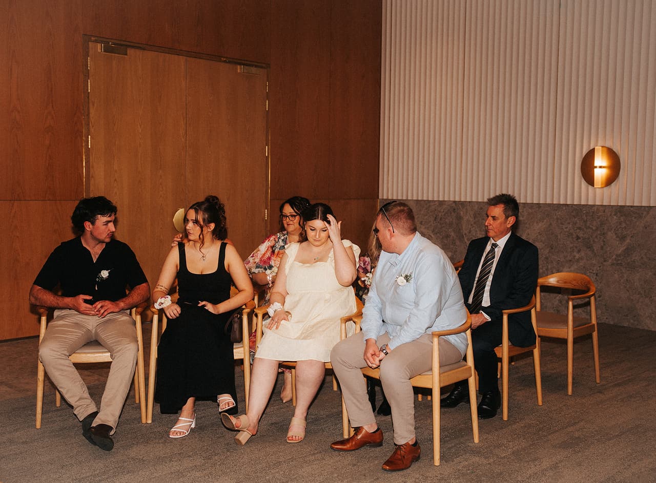 Guests seated along the timber wall of the marriage room, a round wall light beside them
