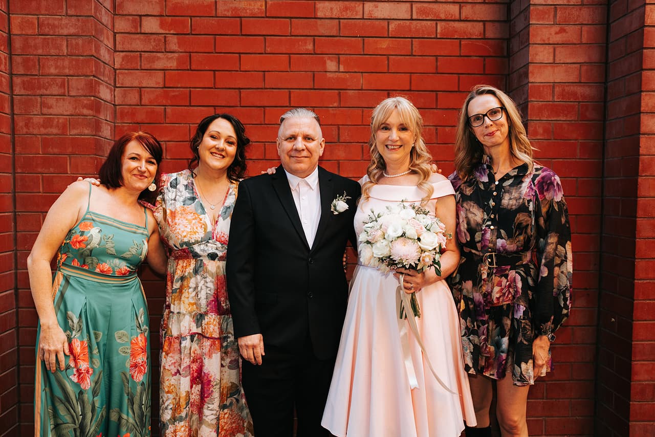 Jon and Terrie with four friends in front of a red brick wall beside the laneway