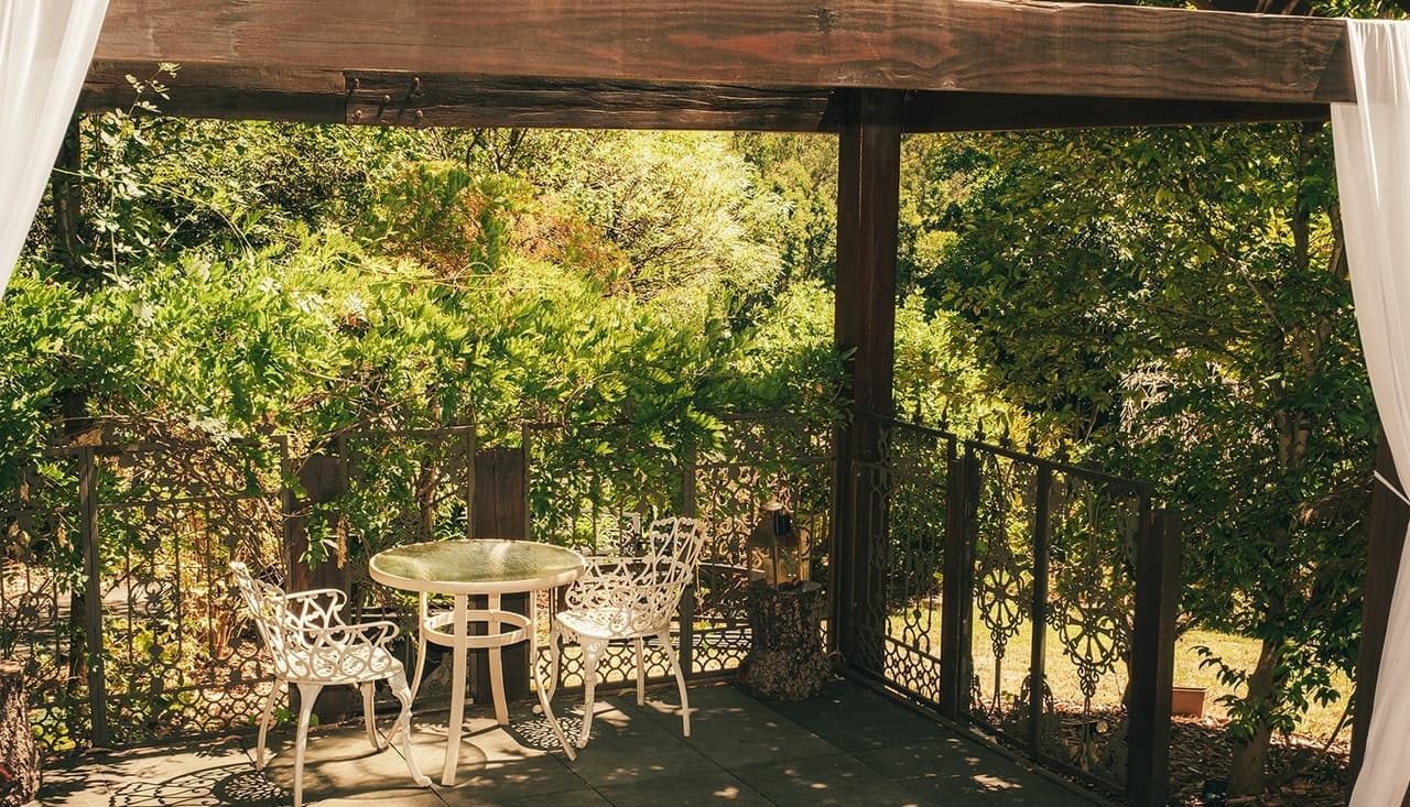 A shaded courtyard under a vine-covered pergola beside the rooms, with white iron garden furniture