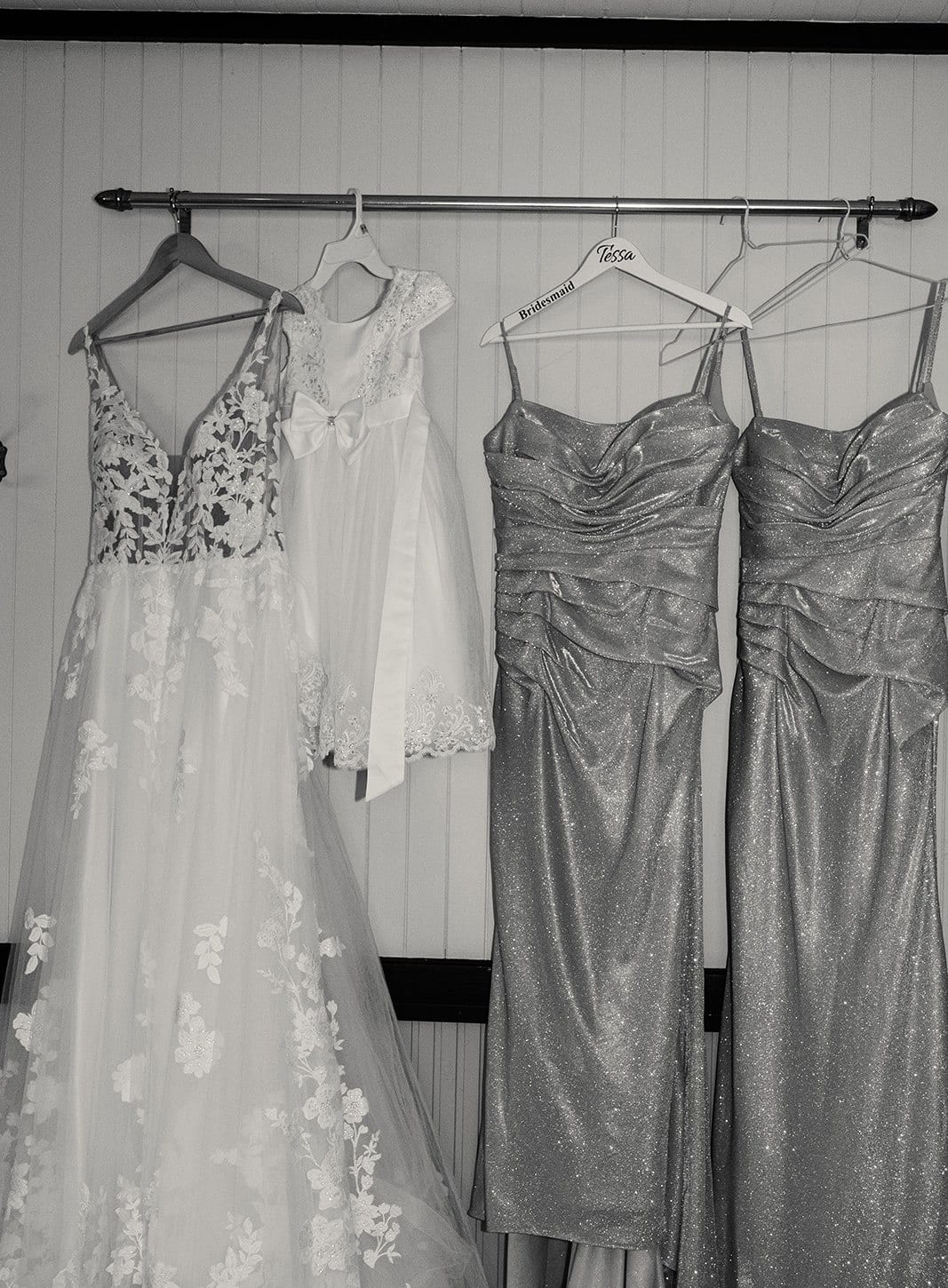 Black and white photo of the bridesmaids’ dresses and a lace gown hanging on the bedroom wall