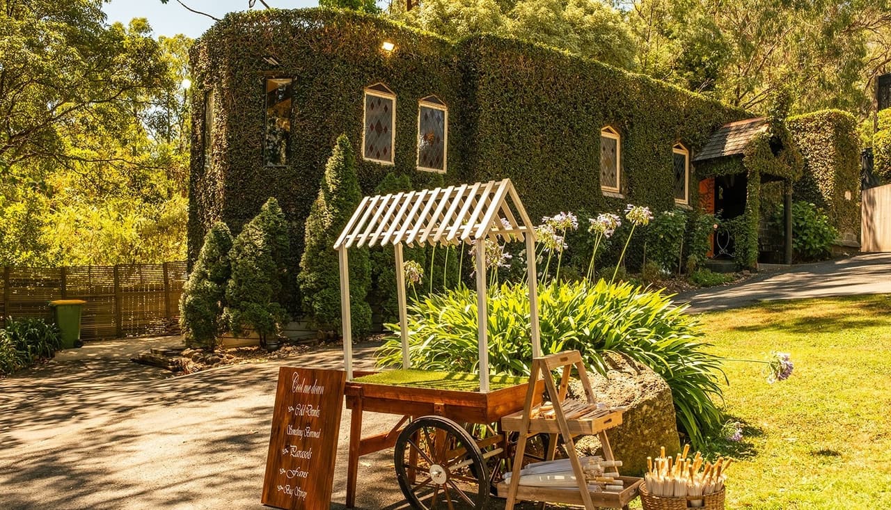 A timber flower cart with drinks and a painted welcome sign by the castle’s ivy walls
