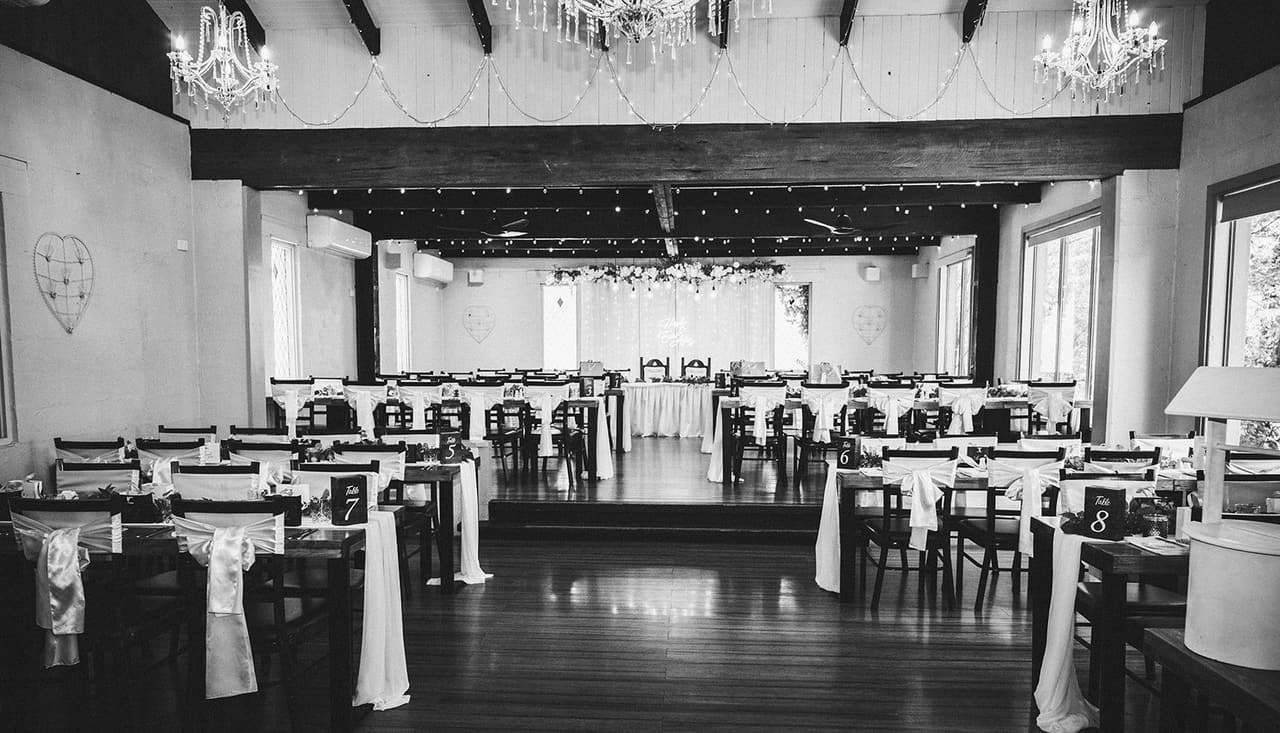 Black and white photo of the reception hall set with long tables and white chair sashes, before the guests arrive