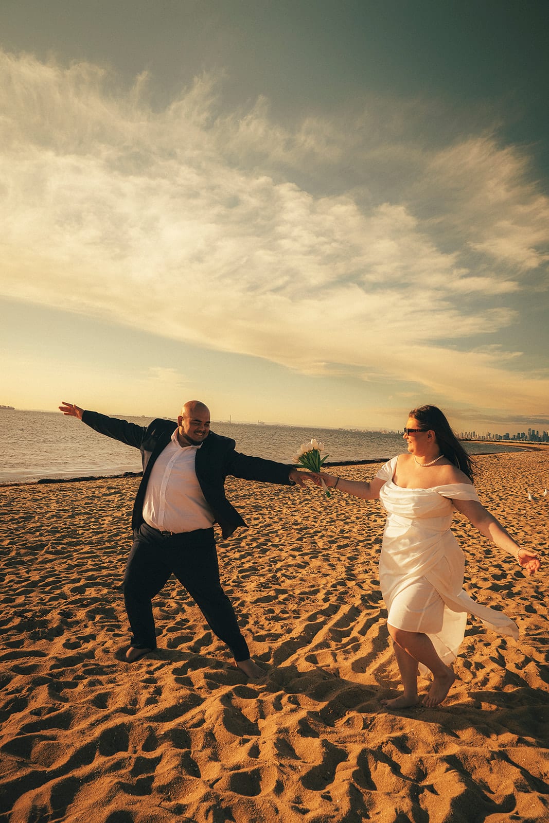 Martina and Diego dancing apart with their arms out on the open sand under a sky full of cloud