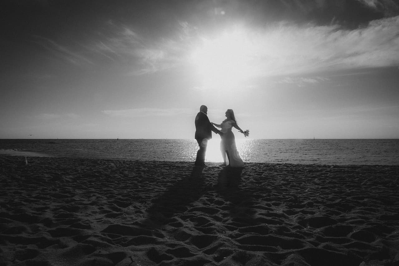Black and white photo of Martina and Diego small on the sand as the sun shines over the bay