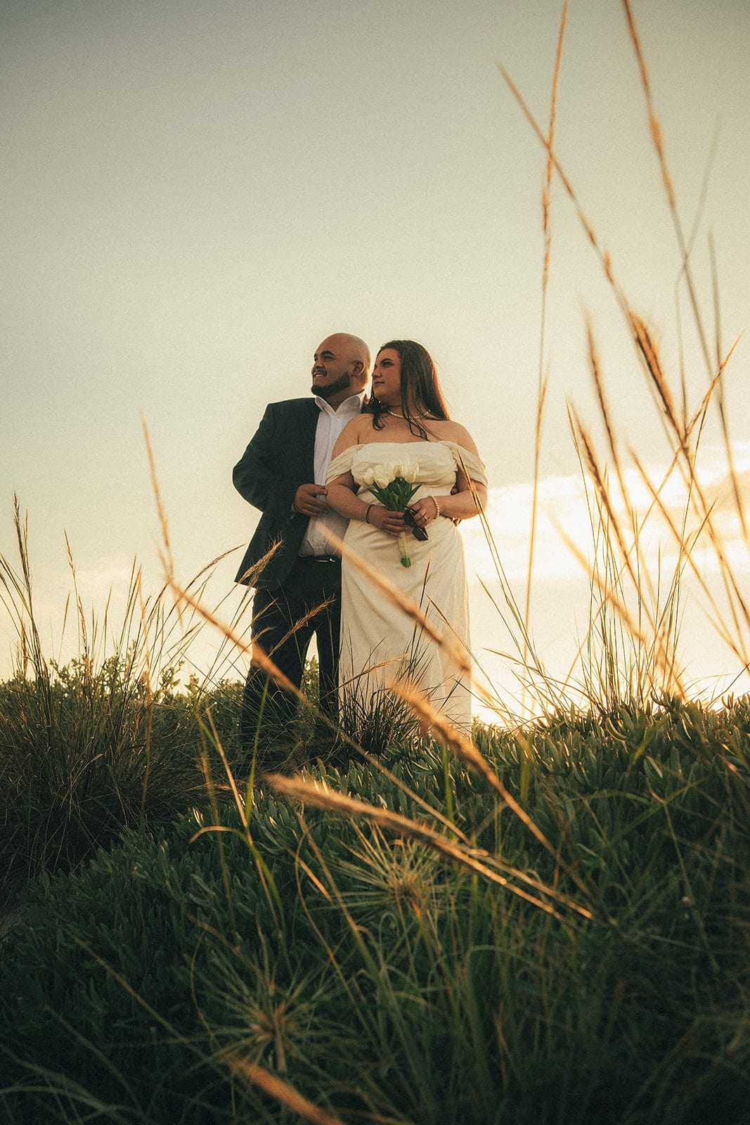 Martina and Diego among the tall grasses on the foreshore, lit from behind by the setting sun