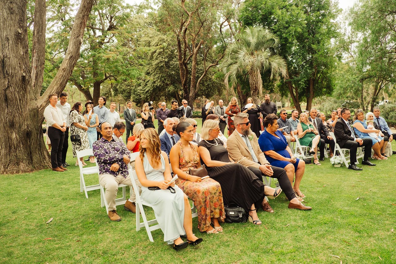 Rows of guests in white folding chairs on the ceremony lawn, palms and gums around them