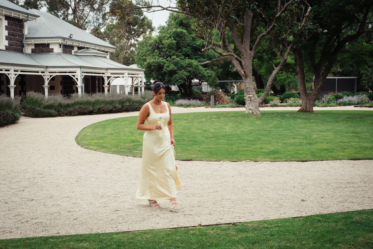 A bridesmaid walking the curved gravel path from the homestead’s veranda to the ceremony