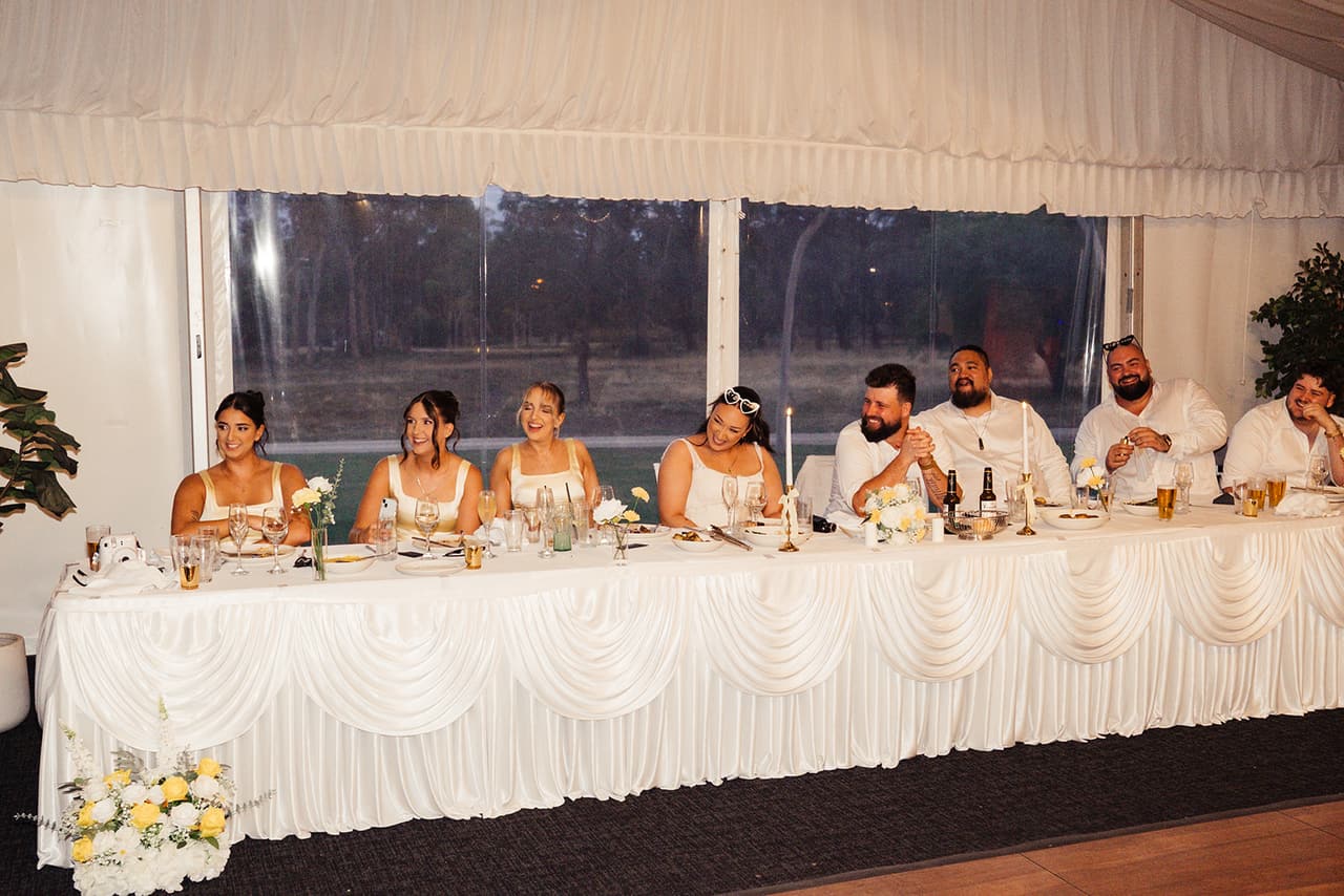The bridal party at the long head table with its white swagged skirt and yellow flowers