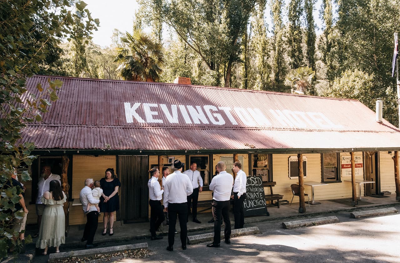 The front of the Kevington Hotel with its name painted on the red iron roof, groomsmen gathering by the door