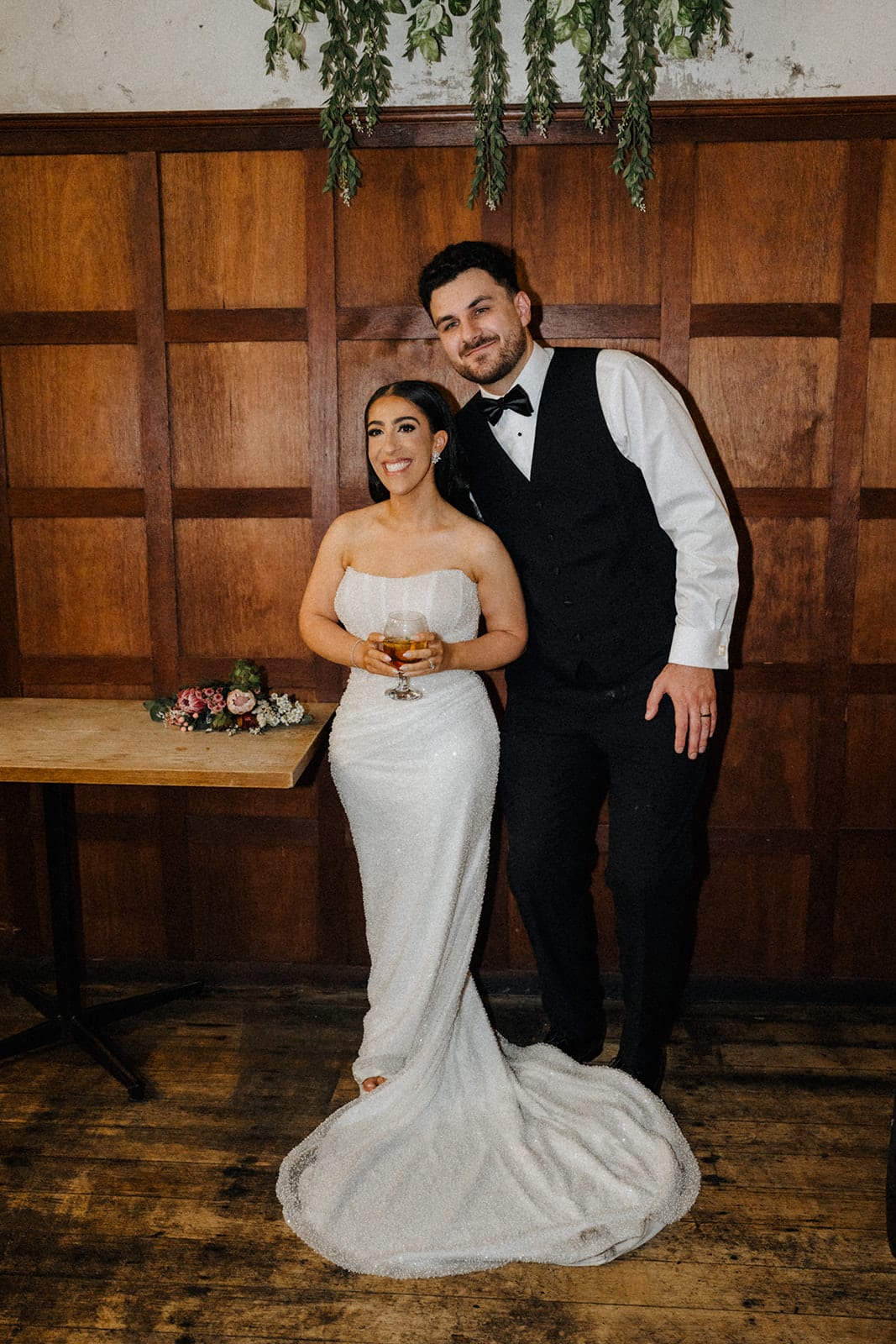 George and Tia in front of the timber panelling, the train of her gown spread over the floorboards
