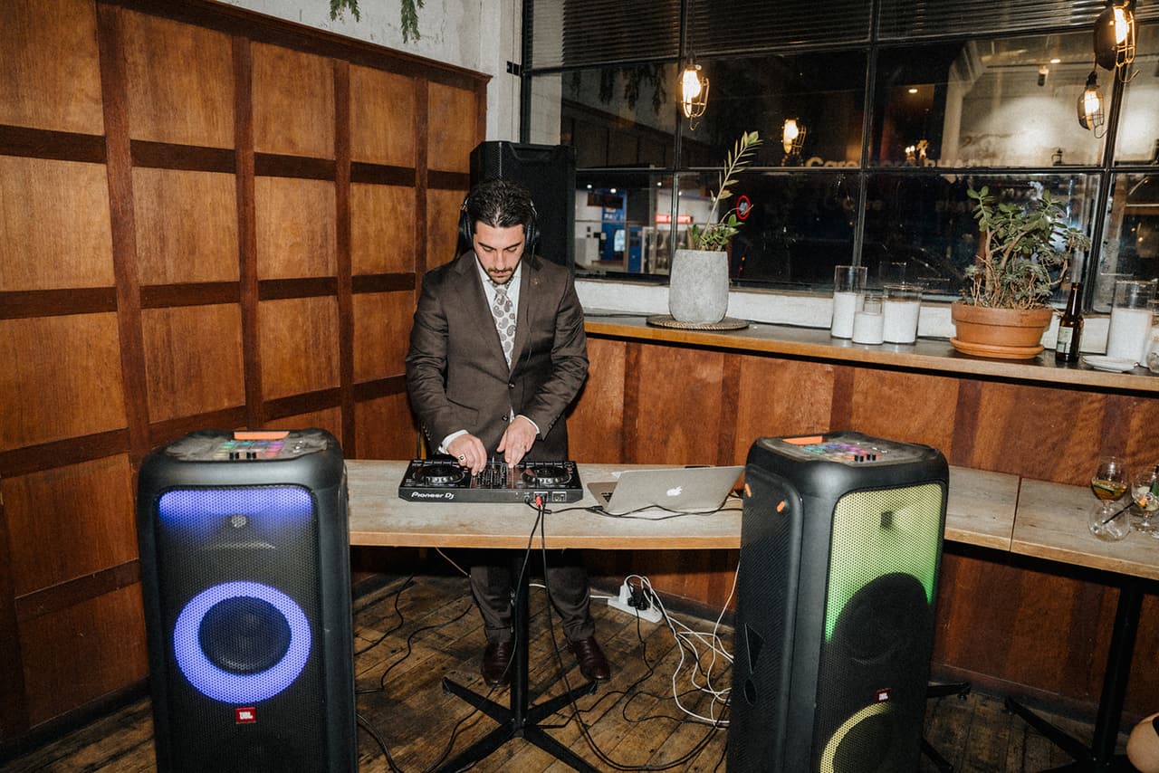 A DJ playing between two glowing speakers in the corner of the timber-panelled room