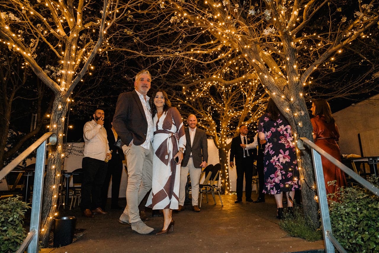 The open courtyard at night, its trees wrapped in fairy lights and guests talking beneath them