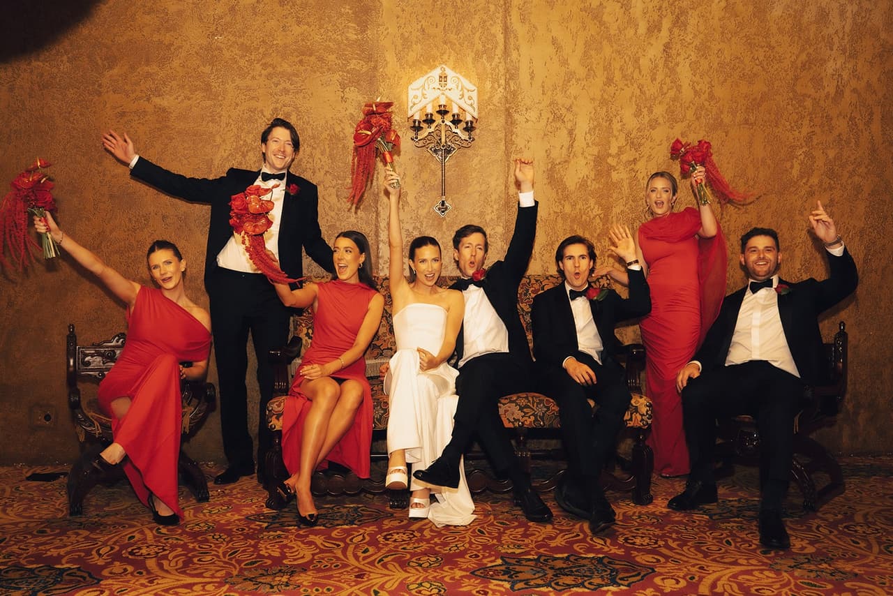 The bridal party in red dresses and dinner suits posing in the Regent Theatre