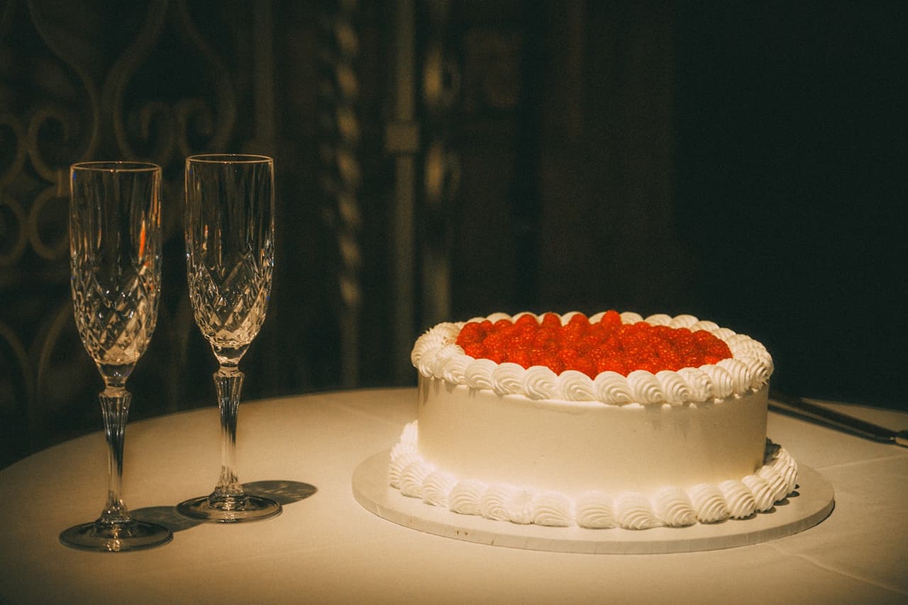 The wedding cake topped with red berries beside two crystal glasses