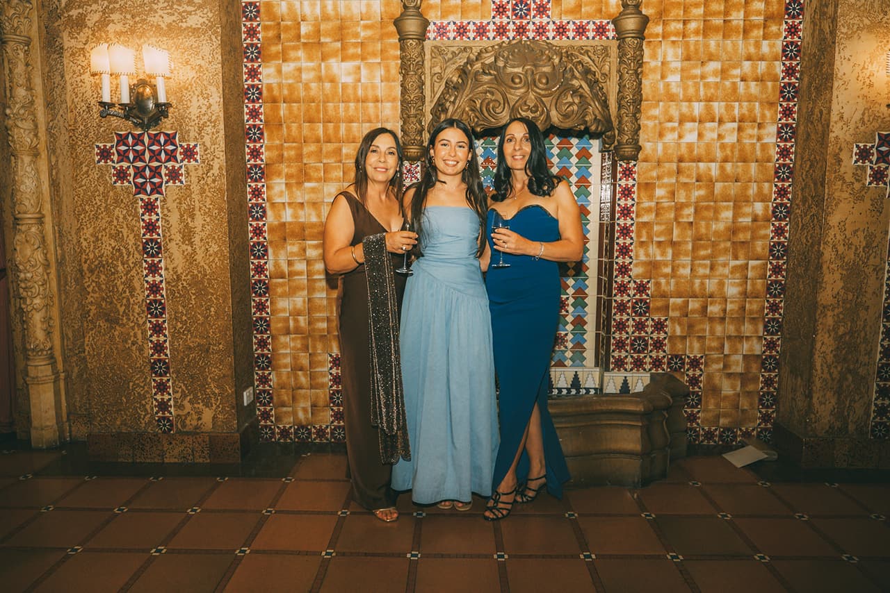 Three guests with drinks in front of the tiled fountain wall in the foyer as they arrive