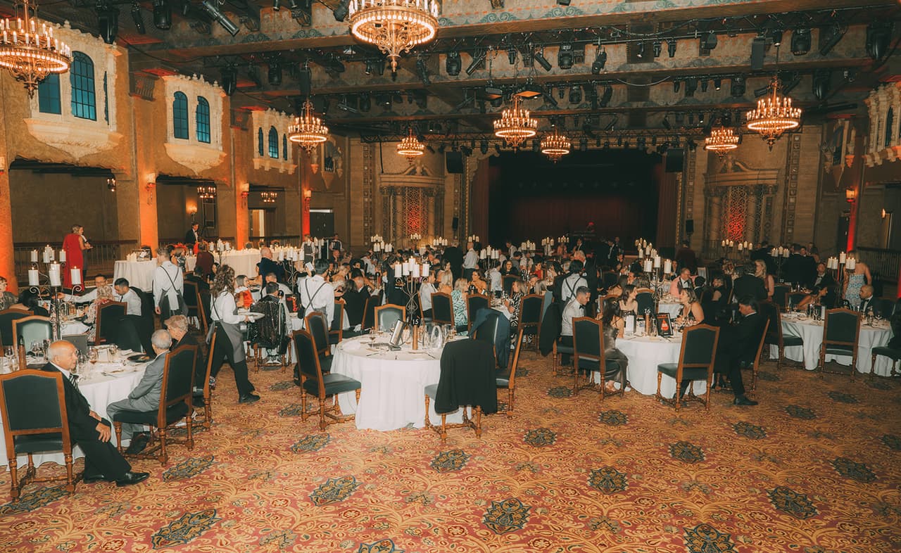 The Plaza Ballroom from the back during dinner, chandeliers hanging over the round tables and the stage at the far end