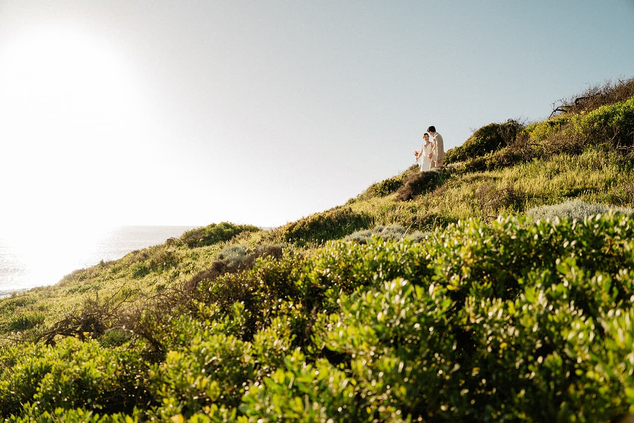 The grassy clifftop with the afternoon sun low over the sea, Sayuri and Shuto small at the top of the slope