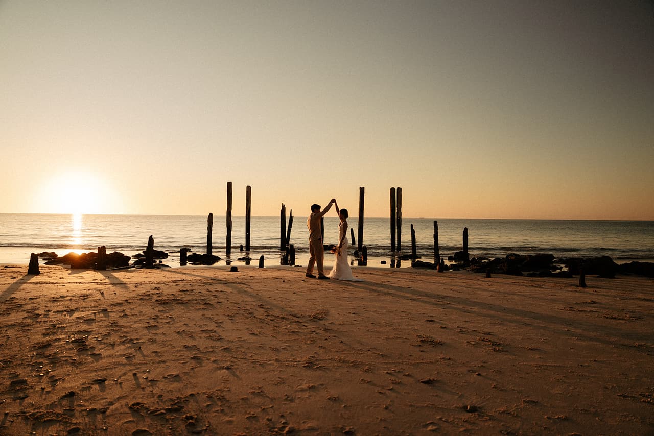 Sayuri and Shuto twirling on the sand in front of the old jetty posts as the sun touches the sea