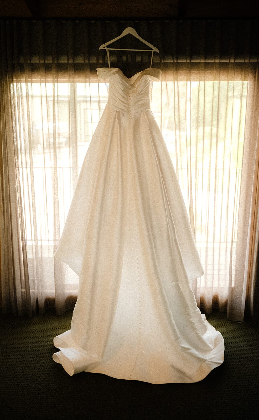 Jessica’s gown hanging in a window of the bridal room, sheer curtains drawn behind it