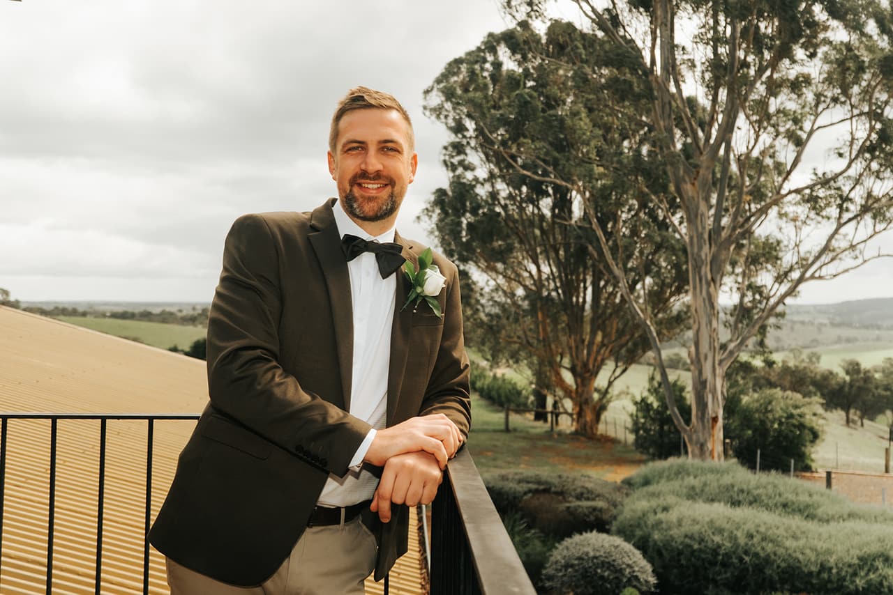 Max leaning on the balcony rail, rounded hedges, paddocks and gum trees below