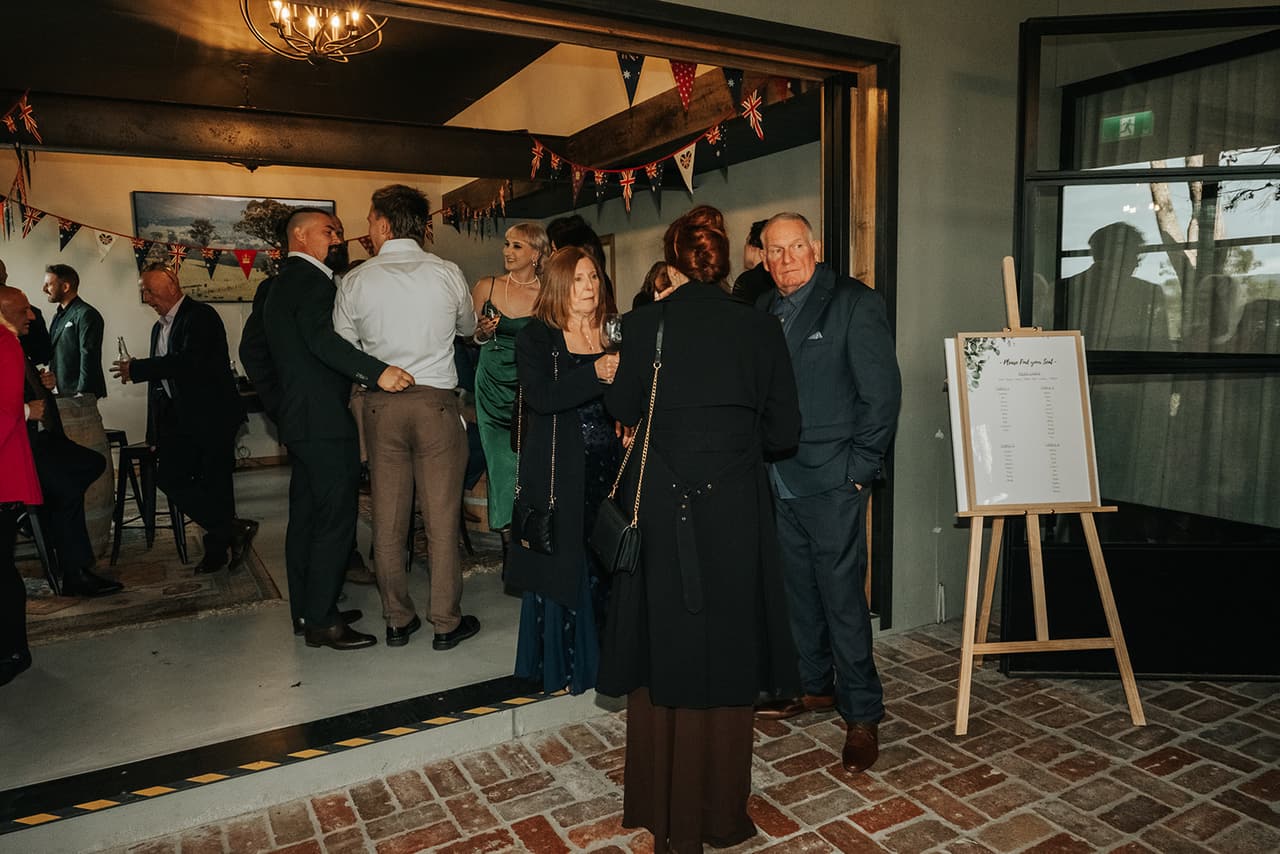 Guests mingling in the room next to the reception, bunting overhead and the welcome sign on an easel