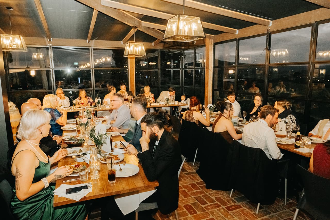 The reception room after dark, guests at long tables under lantern lights and the windows black outside