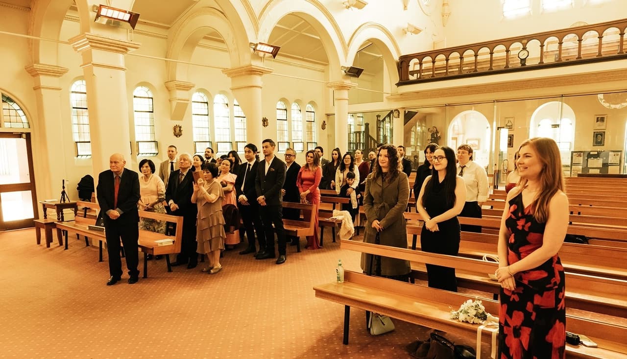 Guests standing in the pews facing the aisle, the choir gallery and its windows behind them