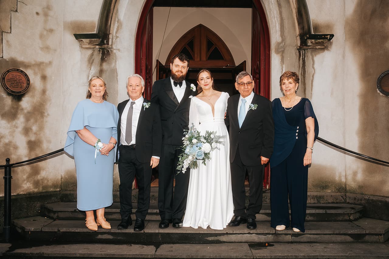 Bianca and Aidan with their parents on the church steps in front of the arched red timber door