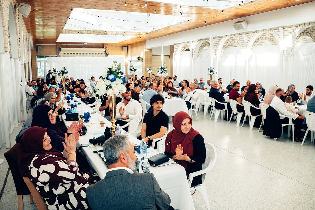 Guests at the long tables clapping after the signing, the hall’s arched brick walls and timber ceiling behind them