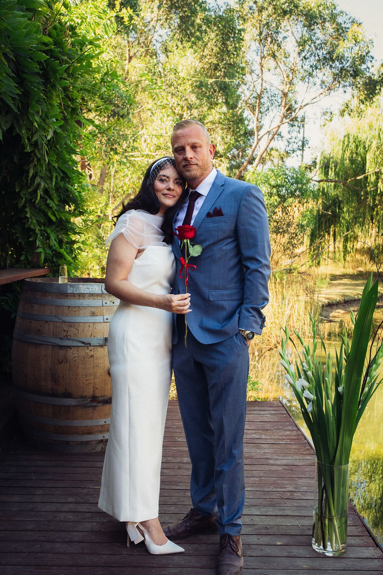 Kim and Ben in the corner of the Boatshed deck beside a wine barrel, willows behind them
