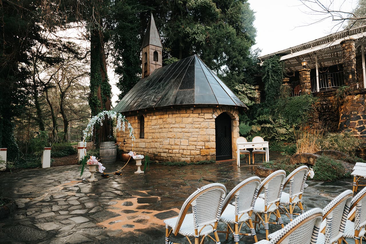 White cane chairs between the stone cottage and the copper-roofed garden chapel