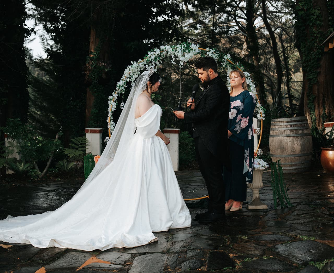Porscha and Jordan under the floral arch with their celebrant, the chapel behind them