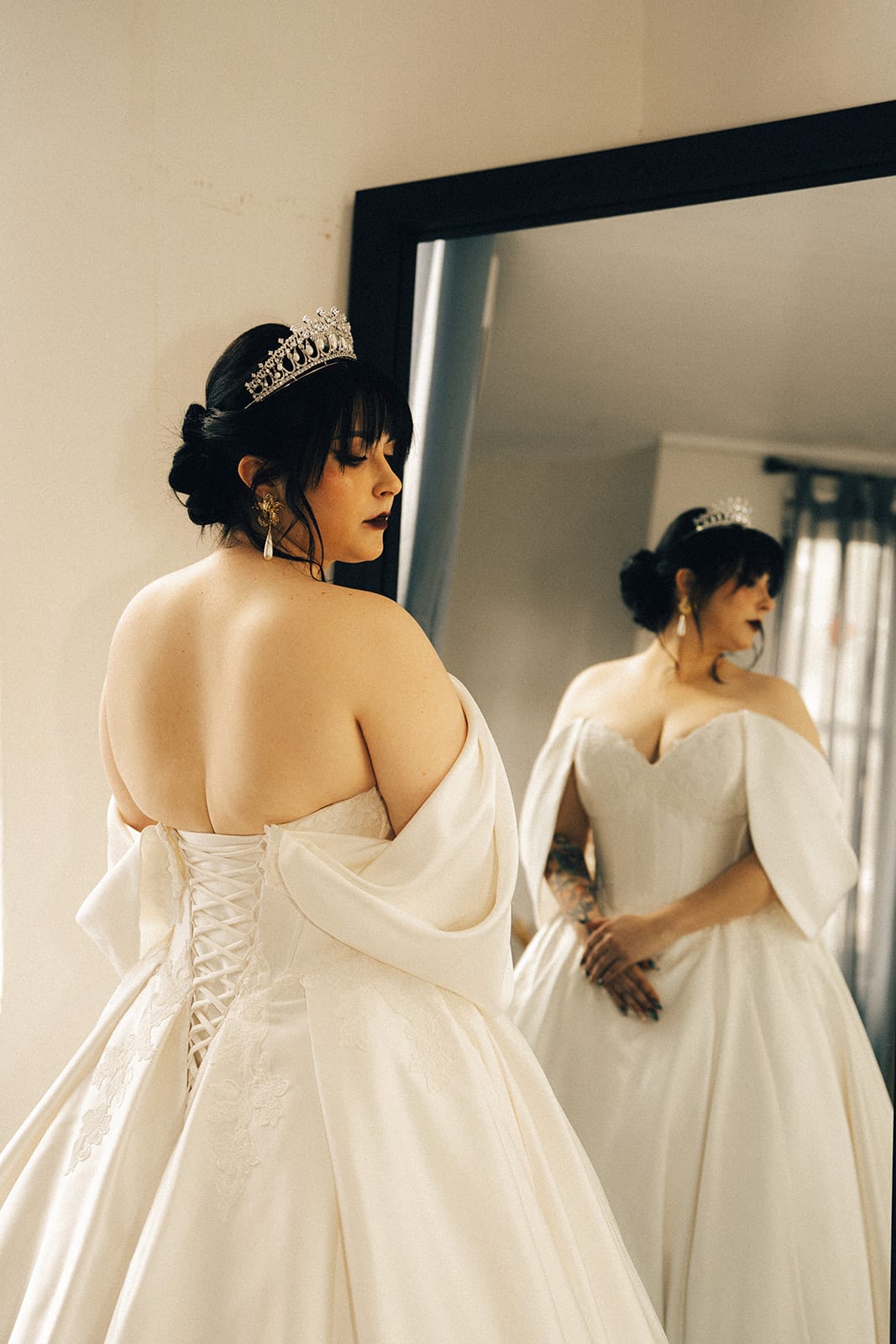 Porscha in a tiara checking her gown in a tall mirror, her reflection beside her