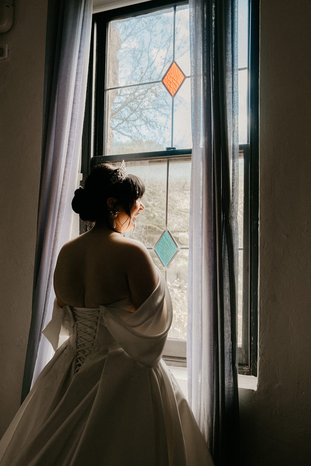 Porscha at a tall leadlight window in the castle, soft light falling on her shoulders
