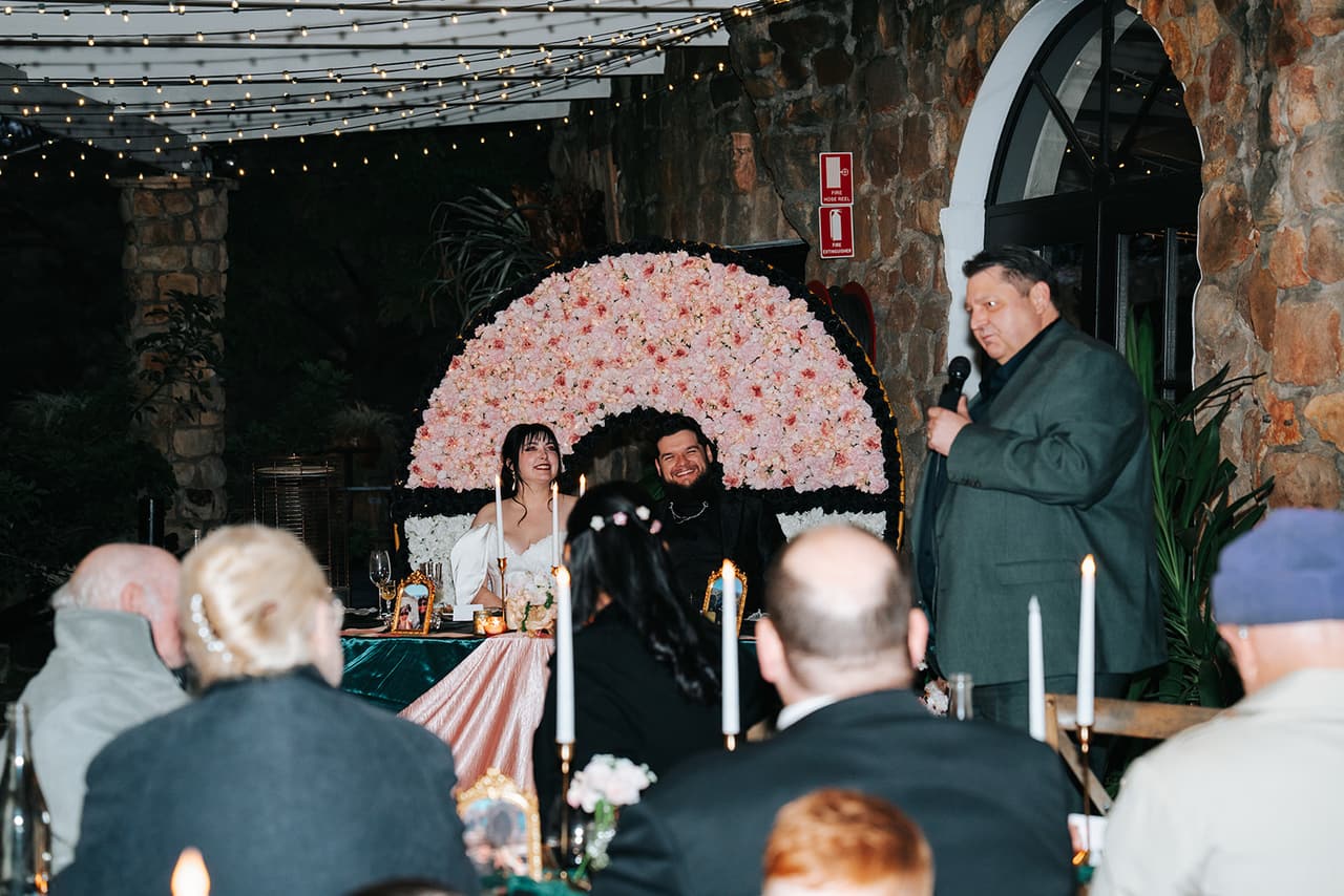 A groomsman giving his speech beside the flower wall while Porscha and Jordan listen from the head table